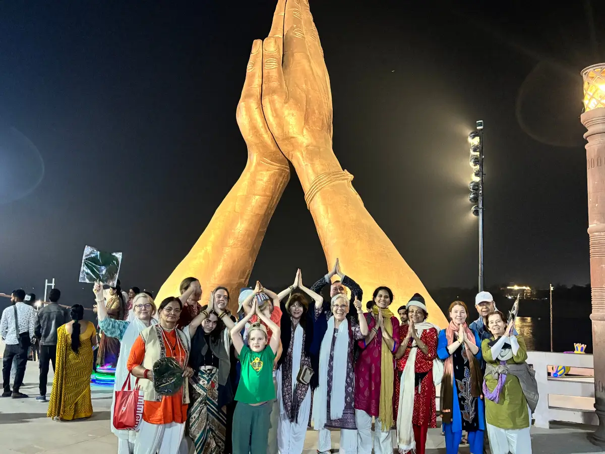 Group posing in front of giant praying hands sculpture at night.