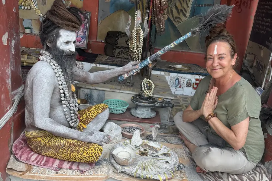 A holy man with ash-covered body sits beside a woman in prayer gesture.